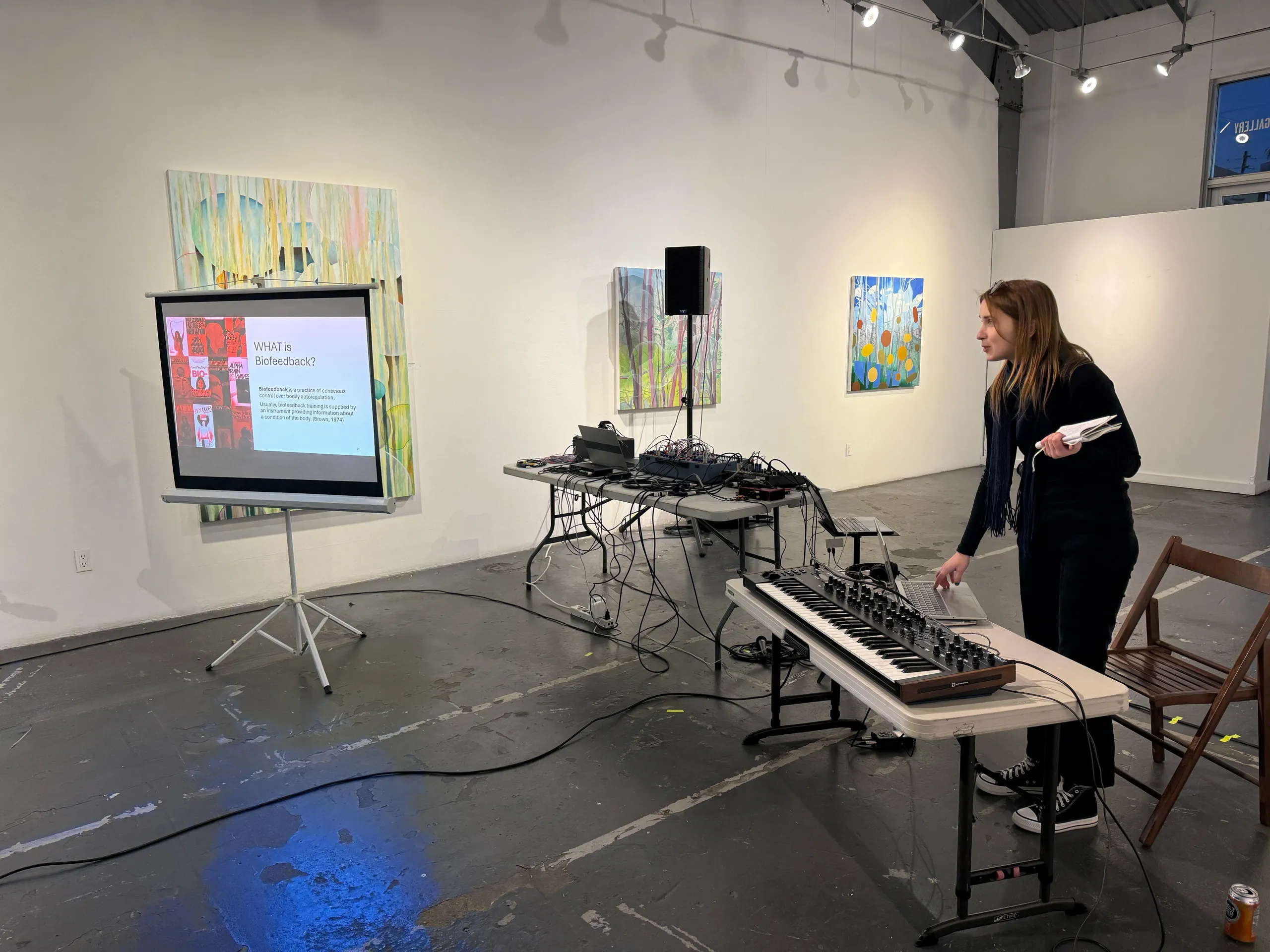 A woman stands in front of a computer, with a table and keyboard visible beside her.